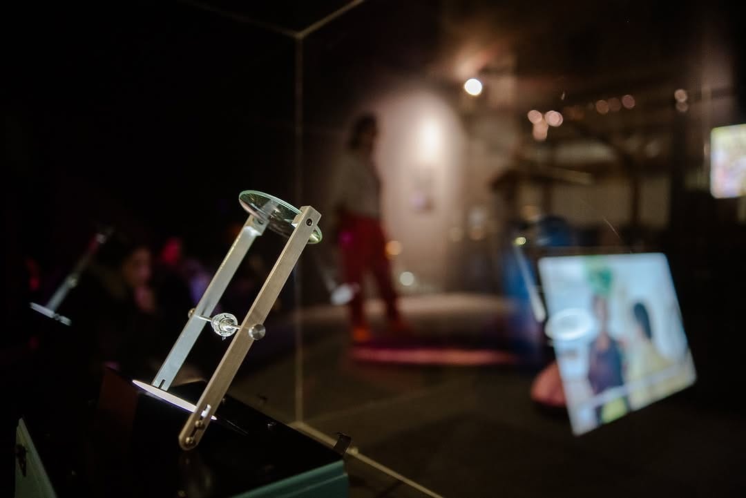 A close-up view of the TX-1 installation, with the vessel backlight, a magnifying glass to observe it, and a reflection on the protective plexiglass that shows one channel of the three-channel video.