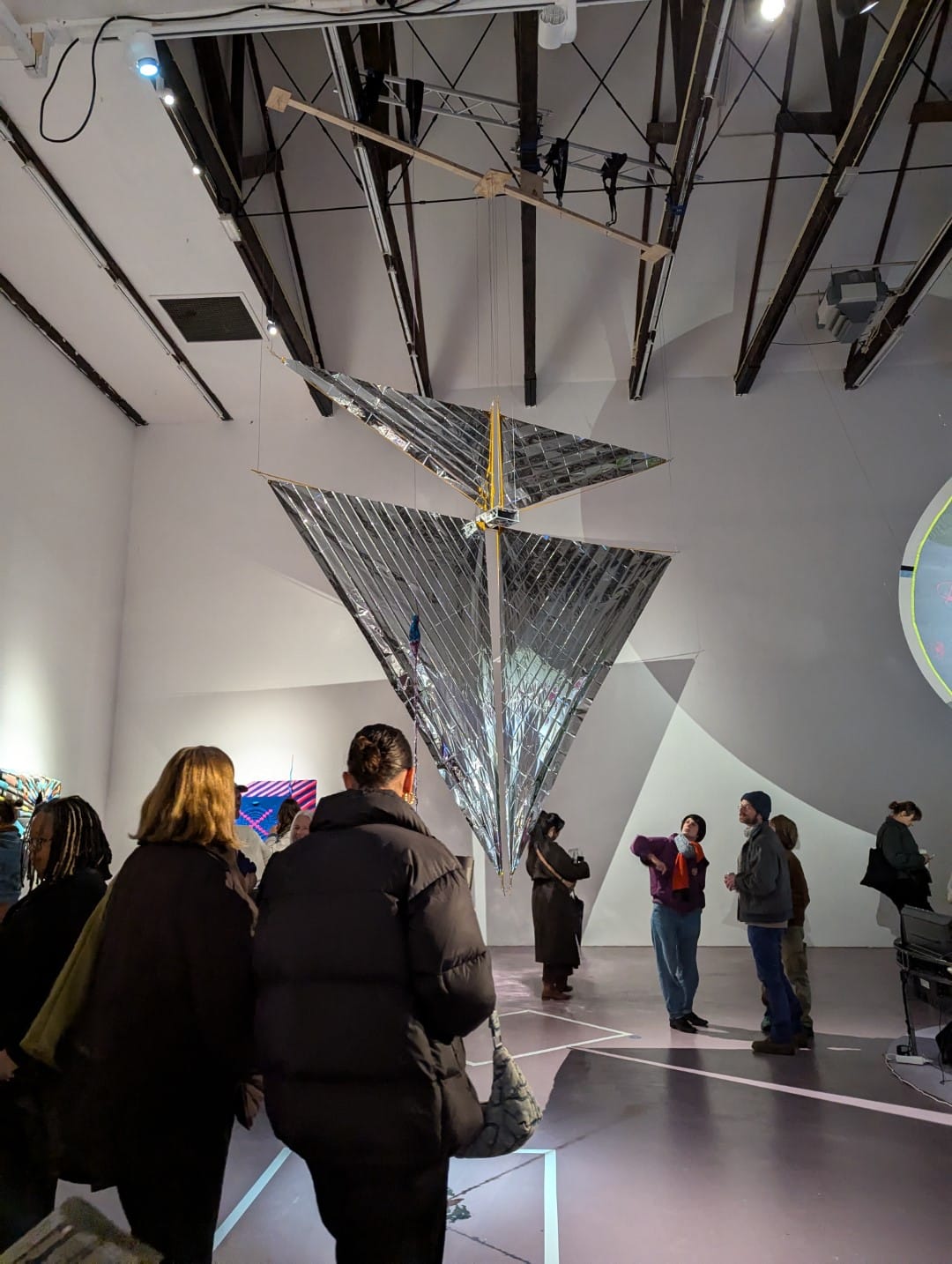 Many people are around TX-1: MOONSHADOW at the opening. Three at the right are looking at it, with their heads tilted upwards.