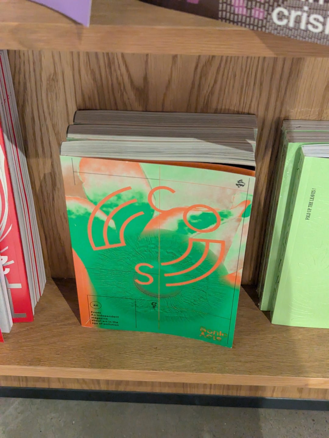 Ecoes #6 issue on the bookshelf at the Tate Modern bookstore. The front cover is a combination of green and orange.