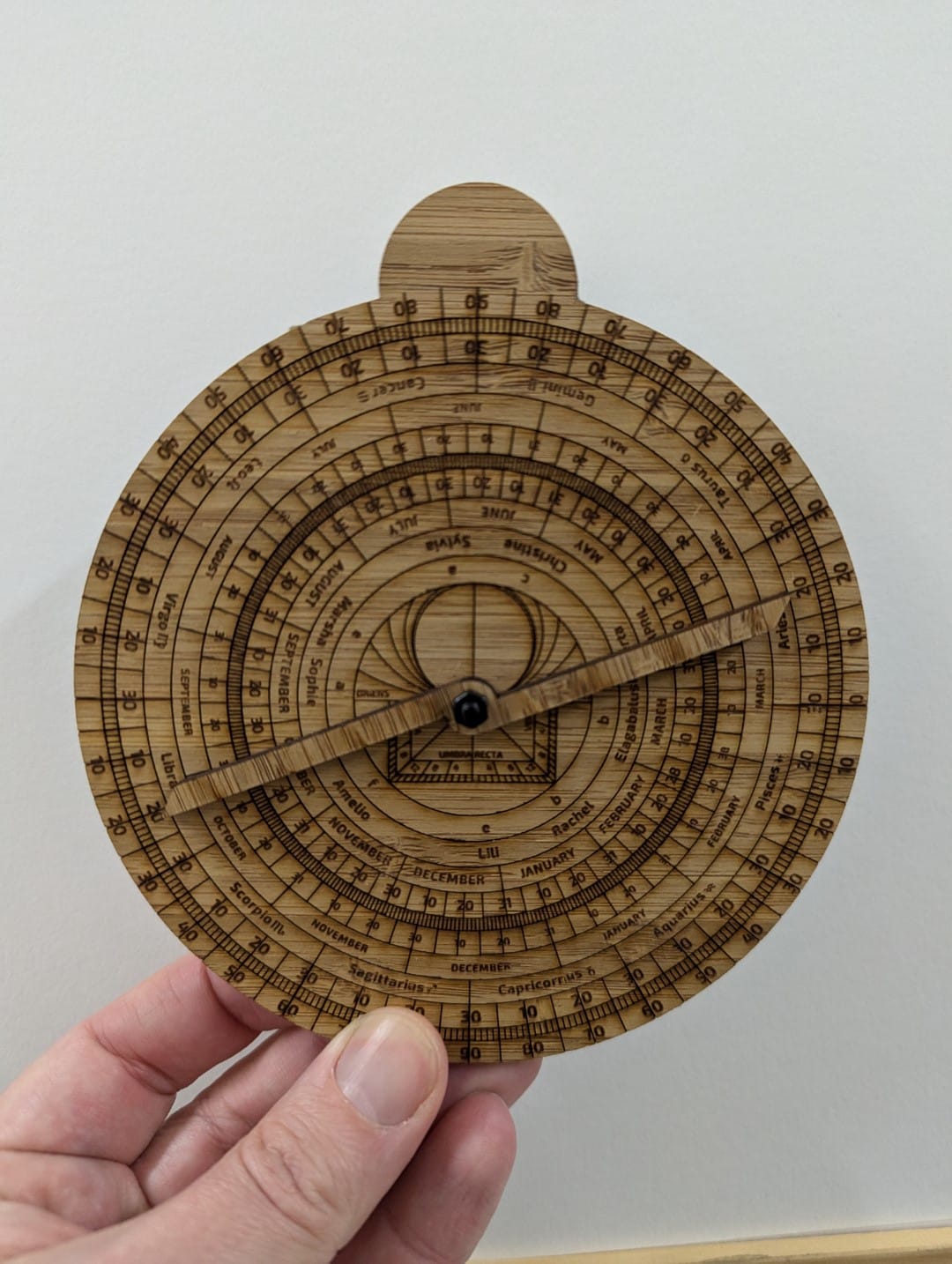 Wooden astrolabe, with laser etched text and markings. Where the usual Christian saints would be I've instead marked the birthdays of important trans people from the past.