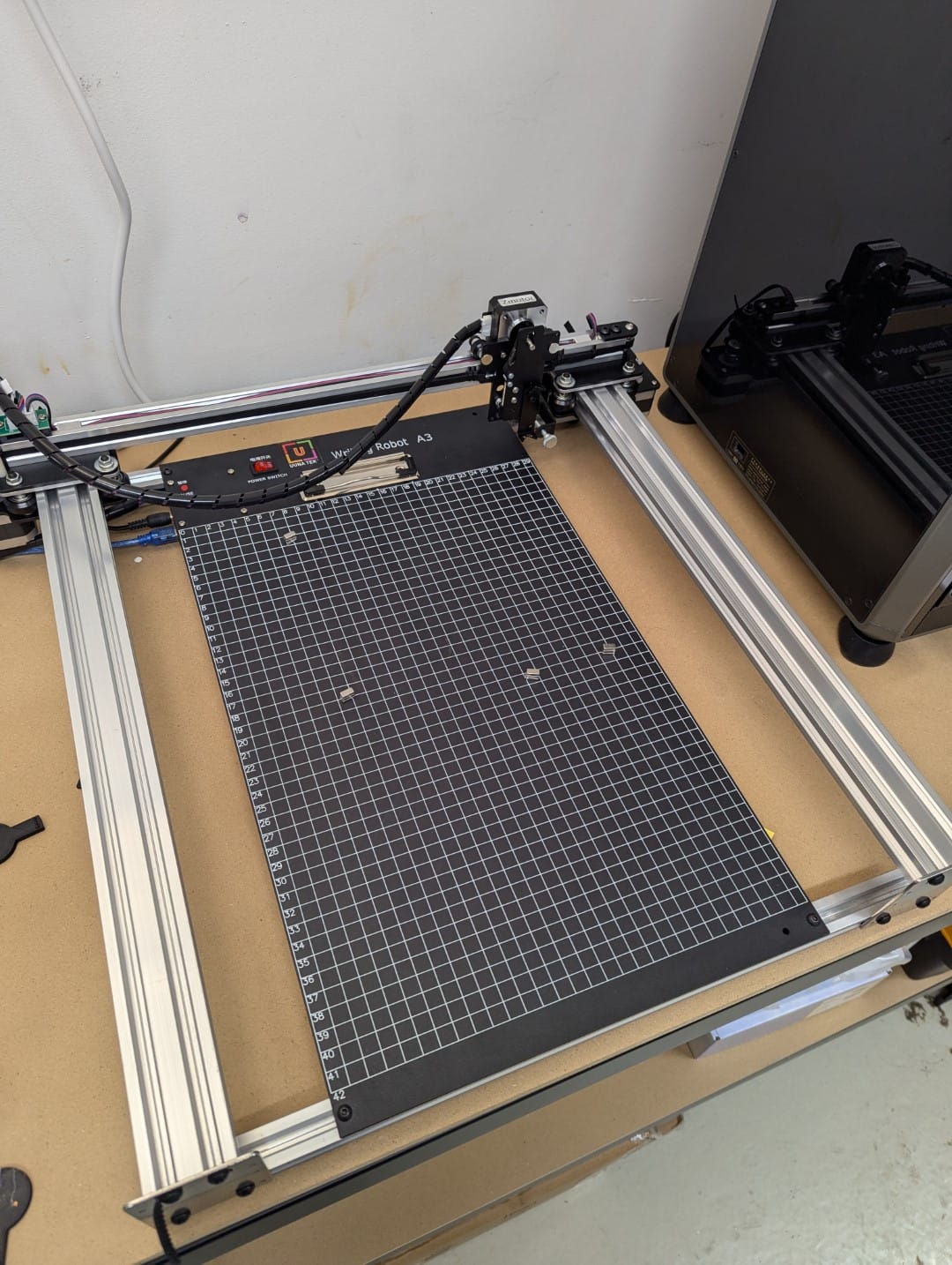 iDraw H A3 drawing robot, with aluminum extrusions for frames, multiple stepper motors, and a black and white plate on which to put paper.